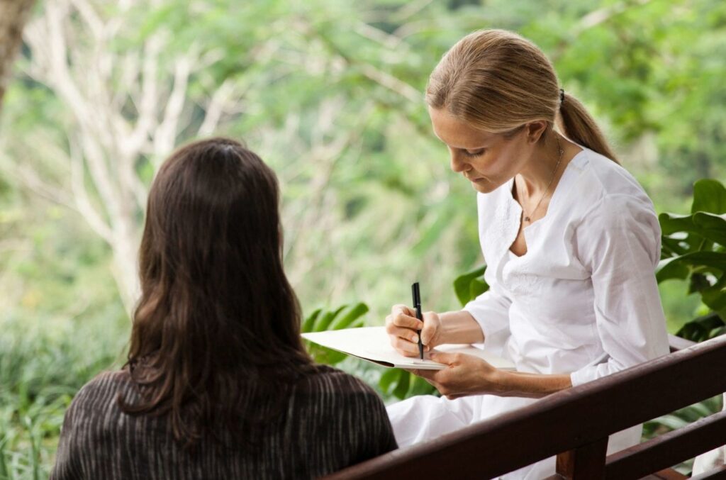 Chuyên gia ghi chép trong buổi trao đổi với khách giữa khung cảnh cây xanh tại COMO Shambhala