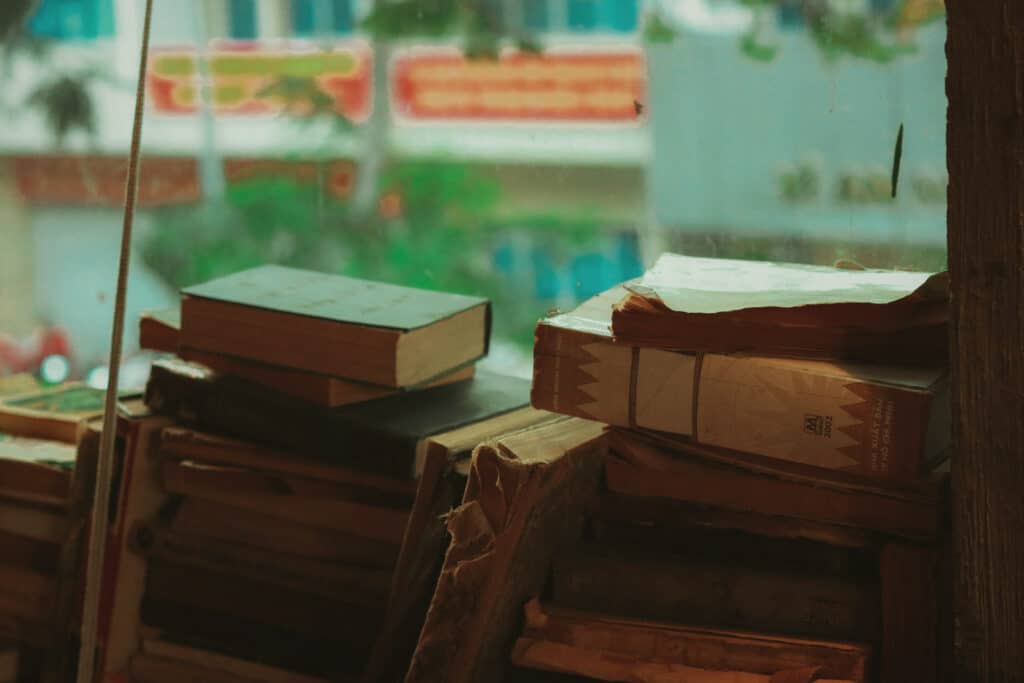 Những chồng sách cũ trên mặt bàn gỗ, phía sau là con phố Việt Nam nhòe màu